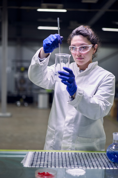 Serious lab woman in glasses and white coat with experimental glass in her hands conducts experiments - Foto, Imagem