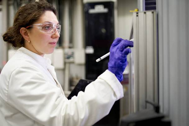 Lab assistent vrouw in witte jas records resultaten in laboratorium - Foto, afbeelding