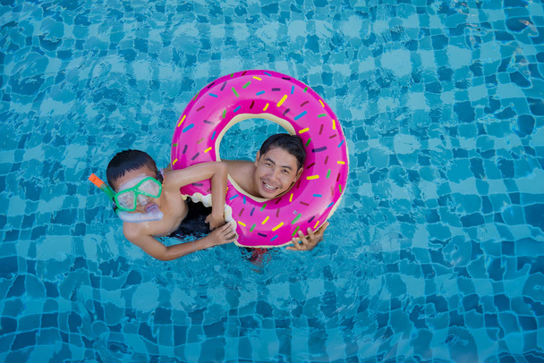 水泳プールに浮かぶリングを泳ぐ男と男の子の眺め - 写真・画像