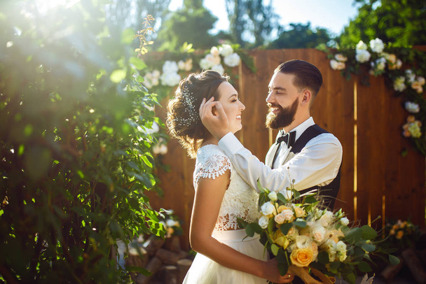 Stylish couple of happy newlyweds posing in the sun. Pretty bride and stylish groom. Romantic moment. Together. Wedding. Marriage. - Foto, imagen