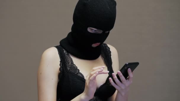 Żona lub dziewczyna w czarnej masce kominiarka używać telefonu komórkowego męża, kobieta z dużymi piersiami ubrana w bieliznę - Materiał filmowy, wideo