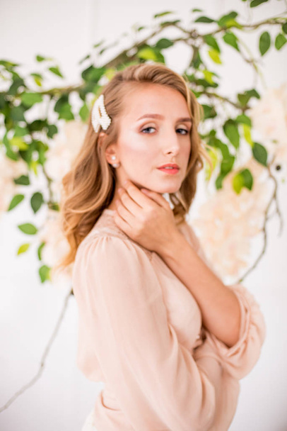 Attractive young girl with blond curly hair and beautiful make-up in a delicate blonde chiffon blouse with white orchids - Φωτογραφία, εικόνα