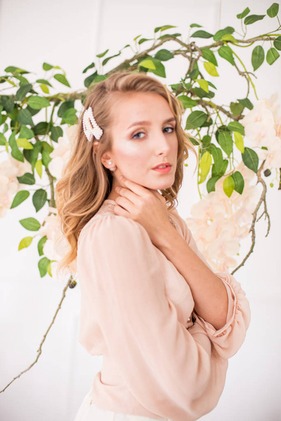Attractive young girl with blond curly hair and beautiful make-up in a delicate blonde chiffon blouse with white orchids - Fotografie, Obrázek