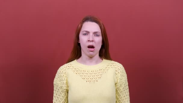 A young woman yawns at the camera. Red background. People sincere emotions, lifestyle concept. - Felvétel, videó