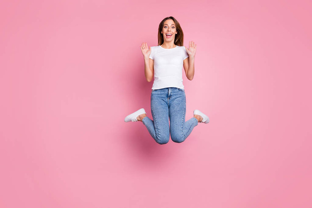 Photo of beautiful crazy lady jumping high enjoy summer sunny weekend days playful mood wear casual white t-shirt jeans sneakers isolated pink color background - Foto, Imagem