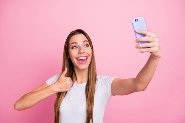 Photo of beautiful lady holding telephone taking selfies raising thumb finger up modern blogger giving feedback wear casual white t-shirt isolated pink color background - Foto, Imagen