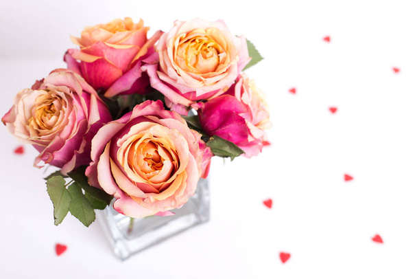 Ροζ τριαντάφυλλα και στολίδια σχήμα καρδιάς σε λευκό φόντο - Φωτογραφία, εικόνα