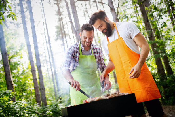 Leisure, food, people and holidays concept. Men cooking meat on barbecue grill at outdoor summer party - Photo, Image