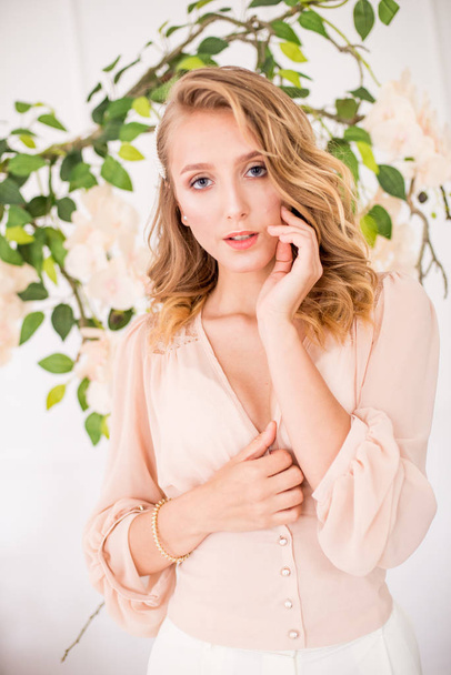 Attractive young girl with blond curly hair and beautiful make-up in a delicate blonde chiffon blouse with white orchids - Fotoğraf, Görsel