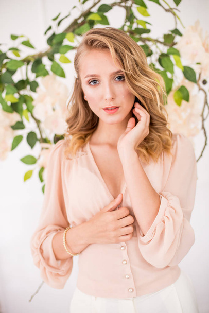 Attractive young girl with blond curly hair and beautiful make-up in a delicate blonde chiffon blouse with white orchids - Zdjęcie, obraz