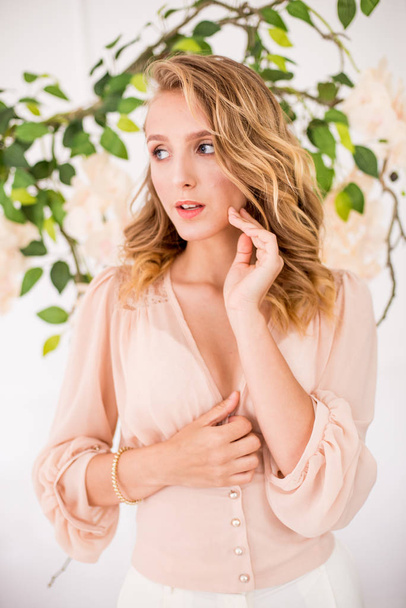 Attractive young girl with blond curly hair and beautiful make-up in a delicate blonde chiffon blouse with white orchids - 写真・画像