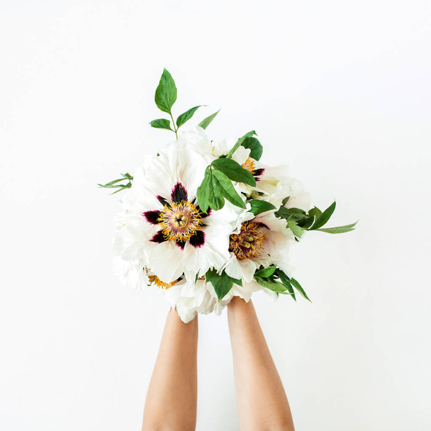 Manos de mujer sosteniendo flores de peonías blancas sobre fondo blanco. Asiento plano, vista superior. Composición floral mínima
. - Foto, Imagen