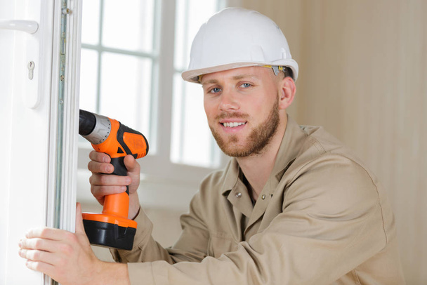 young male contractor using drill on pvc door - Φωτογραφία, εικόνα
