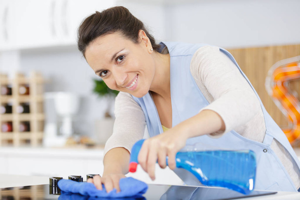 happy woman cleaning kitchen cloth and spray in kitchen - Foto, afbeelding