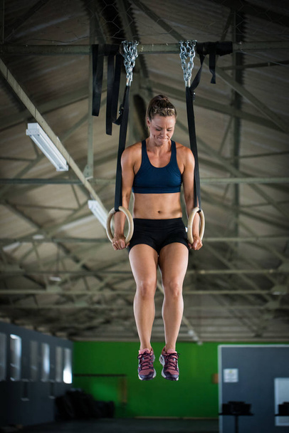 Женщина фитнес-модель делает кросс-фитнес тренировки на более головы кольца в тренажерном зале, подтягивая себя
 - Фото, изображение