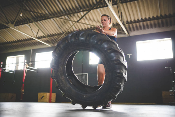 Female fitness model doing cross fit exercise with a massive tyre in a gym - 写真・画像
