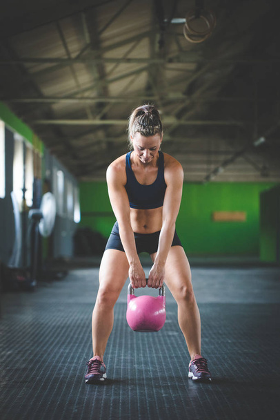 Female fitness model doing kettle bell exercises in a cross fit gym - Photo, image