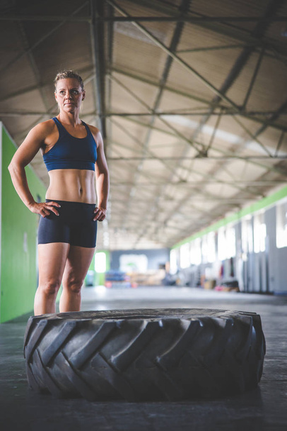 Female fitness model doing cross fit exercise with a massive tyre in a gym - Foto, Bild