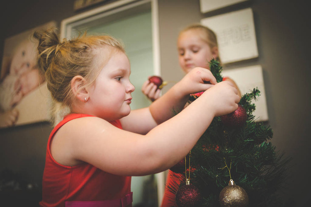 Close up image of two young girls / sisters, decorating a Christmas tree for the holidays - Photo, Image