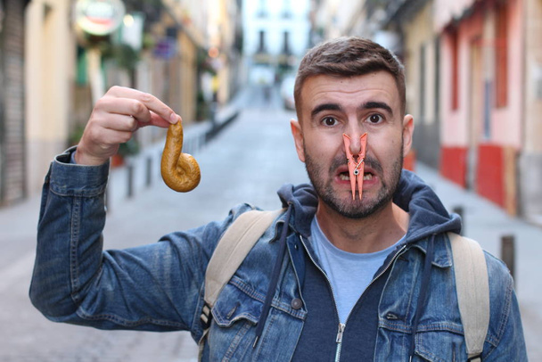close-up portret van knappe jongeman met wasknijper op neus houden poep op straat - Foto, afbeelding