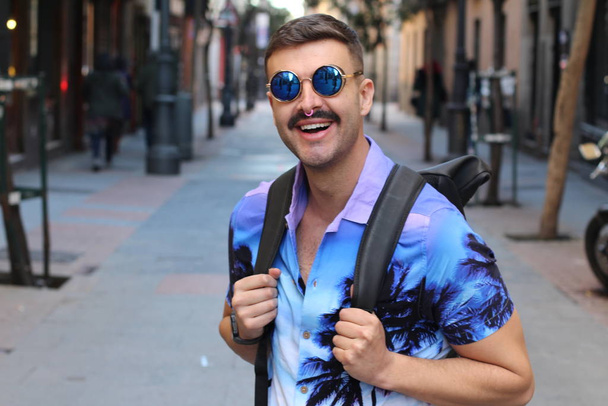 portrait de près d'un beau jeune homme vêtu d'une chemise et de lunettes de soleil de couleur violette dans la rue - Photo, image