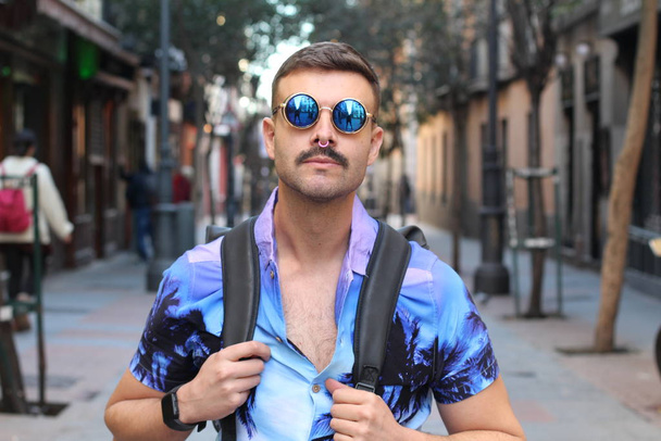 portrait de près d'un beau jeune homme vêtu d'une chemise et de lunettes de soleil de couleur violette dans la rue - Photo, image