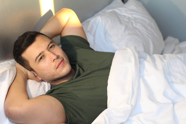 close-up portrait of handsome young man relaxing in bed at home - Foto, Imagen