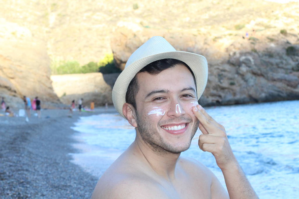 portrait de près d'un beau jeune homme en chapeau de paille bronzant avec crème de spf - Photo, image