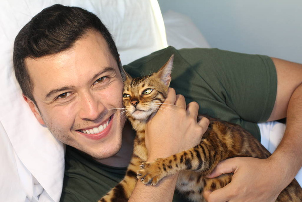 κοντινό πορτραίτο ενός όμορφου νεαρού άντρα που χαλαρώνει στο κρεβάτι με τη γάτα του στο σπίτι - Φωτογραφία, εικόνα