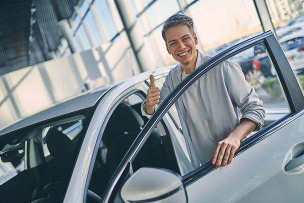 Ευτυχισμένος άνθρωπος χαίρεται αγοράζοντας ένα νέο αυτοκίνητο στο showroom. - Φωτογραφία, εικόνα