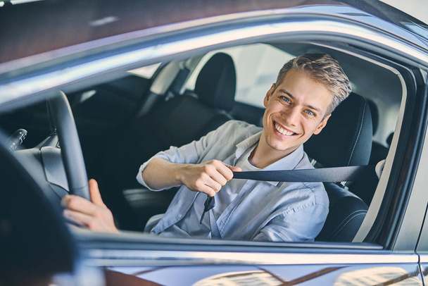 Caucasian man sitting in a new car hold a safety belt.  - Фото, изображение