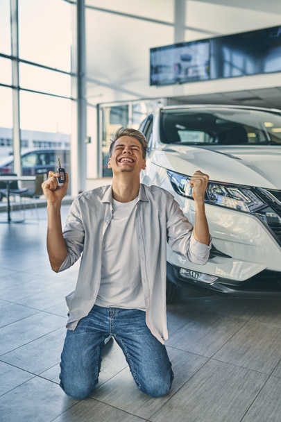 Homem feliz ficar de joelhos regozijando-se comprar um carro novo no showroom
. - Foto, Imagem