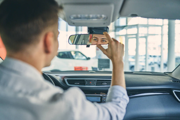 Stylish caucasian man testing a rear view mirror in new car. - Photo, Image