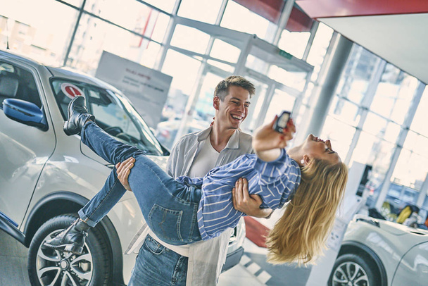 Ευτυχισμένο ζευγάρι που διασκεδάζει μετά την αγορά ενός νέου αυτοκινήτου. - Φωτογραφία, εικόνα