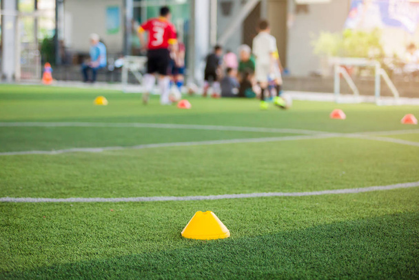Μαρκαδόρος Cone σε πράσινο τεχνητό χλοοτάπητα με θολή παιδί ποδόσφαιρο παίζουν - Φωτογραφία, εικόνα
