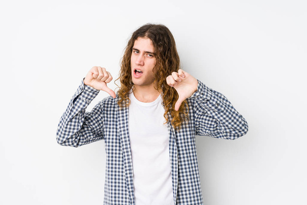 Молодий довге волосся чоловік позує ізольовано, показуючи великий палець вниз і виражаючи неприязнь
. - Фото, зображення