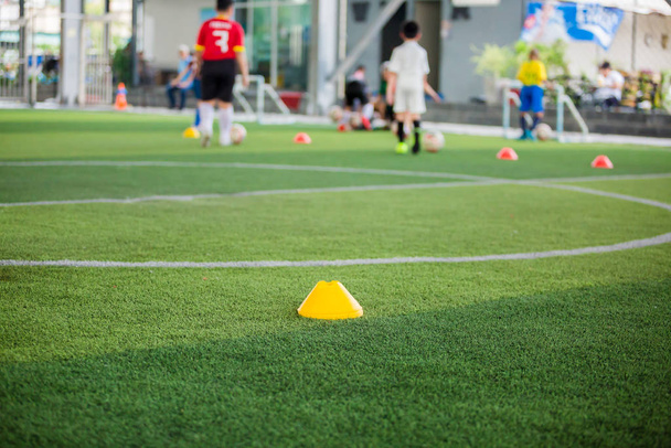 Cono marcador en césped artificial verde con juego de fútbol infantil borrosa
 - Foto, Imagen