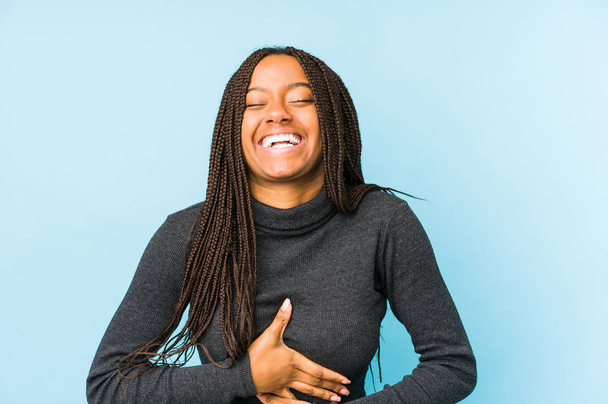 Junge Afroamerikanerin isoliert auf blauem Hintergrund lacht fröhlich und hat Spaß dabei, die Hände auf dem Bauch zu halten. - Foto, Bild