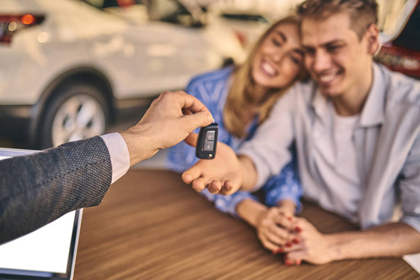 Happy cheerful girl getting a car key with handsome man in showr - Foto, Imagem