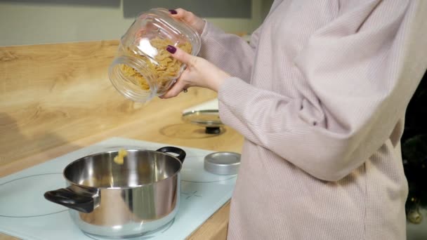 mujer cocina la cena y vierte pasta en una cacerola en la estufa
 - Imágenes, Vídeo