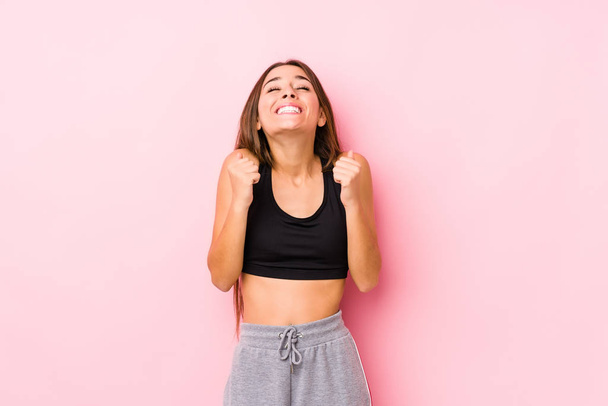 Young caucasian fitness woman posing in a pink background raising fist, feeling happy and successful. Victory concept. - Photo, Image