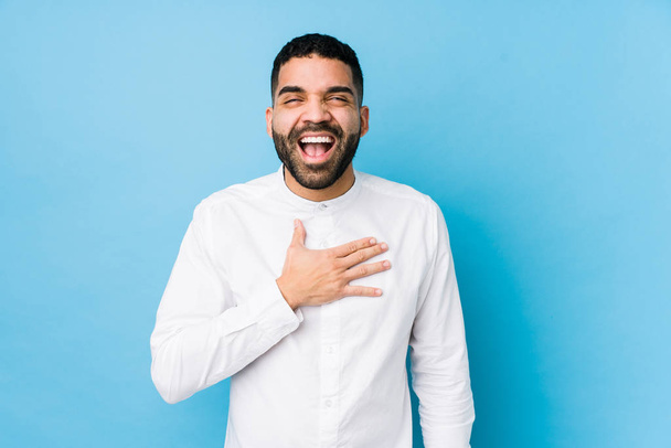 Young latin man against a blue  background isolated laughs out loudly keeping hand on chest. - Photo, image