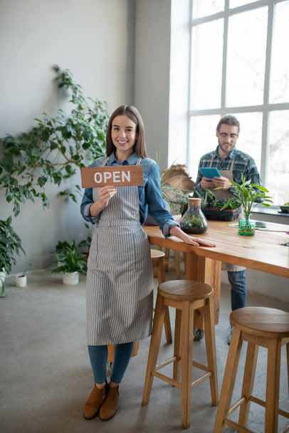 Smiling woman in apron holding an open sign - Foto, afbeelding