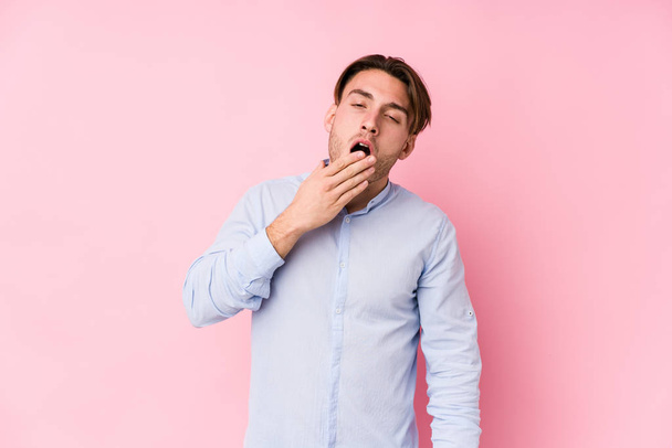 Joven hombre caucásico posando en un fondo rosa bostezo aislado mostrando un gesto cansado cubriendo la boca con la mano. - Foto, imagen
