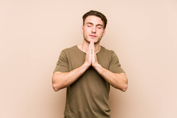 Young caucasian man posing isolated holding hands in pray near mouth, feels confident. - Photo, Image