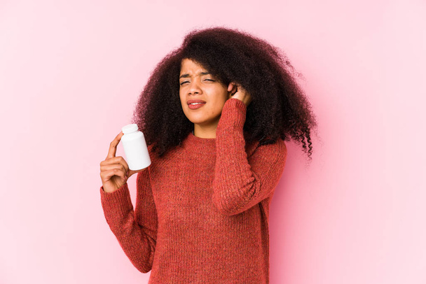 Young afro woman holding a vitamins isolated Young afro woman holding a vitaminscovering ears with hands. - Foto, afbeelding