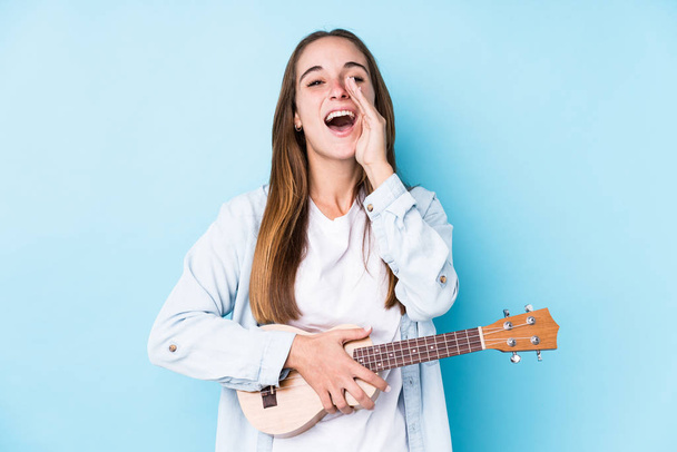 Young caucasian woman holding a ukelele isolated shouting excited to front. - 写真・画像