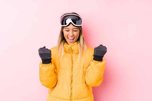 ピンクの背景にスキー服を着た若い白人女性が気楽で興奮して応援しています。勝利のコンセプト. - 写真・画像