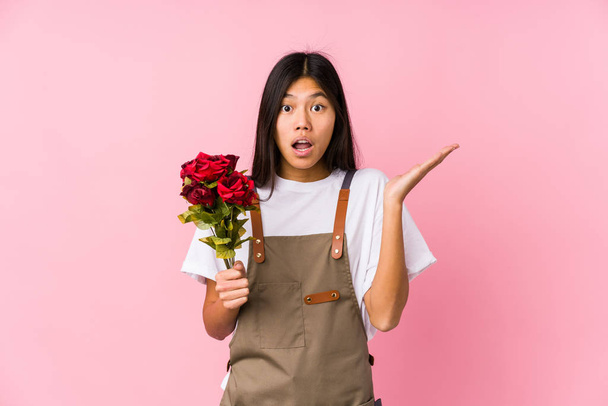 Молодая китайская садовница, держащая в руках розы, удивлена и потрясена
. - Фото, изображение