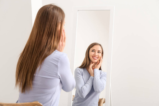 Όμορφη νεαρή γυναίκα κοιτάζει στον καθρέφτη στο σπίτι - Φωτογραφία, εικόνα